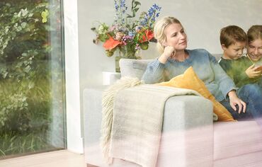 Family relaxing in sofa behind big glass window.